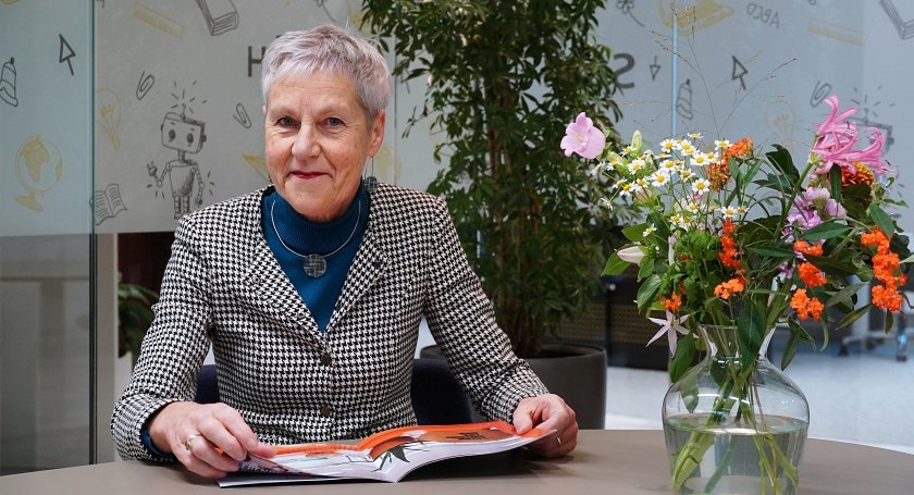 Een foto van SCOH-directeur Joke Snippe. Ze lacht vriendelijk, zit aan een tafel en heeft de Strategische Koers in haar handen. 